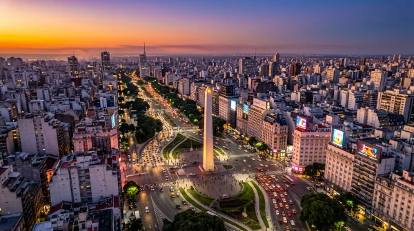 Obelisco de Buenos Aires durante la hora dorada. El cielo muestra un degradado espectacular de naranja, púrpura y azul profundo. La ciudad se extiende debajo con luces urbanas empezando a brillar.